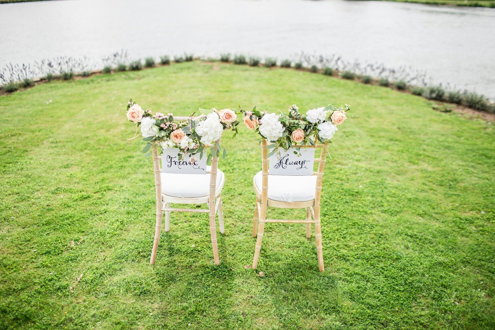 Trauung in Berlin und Brandenburg Zwei dekorierte Stühle mit Blumenarrangements, Blick auf einen See.